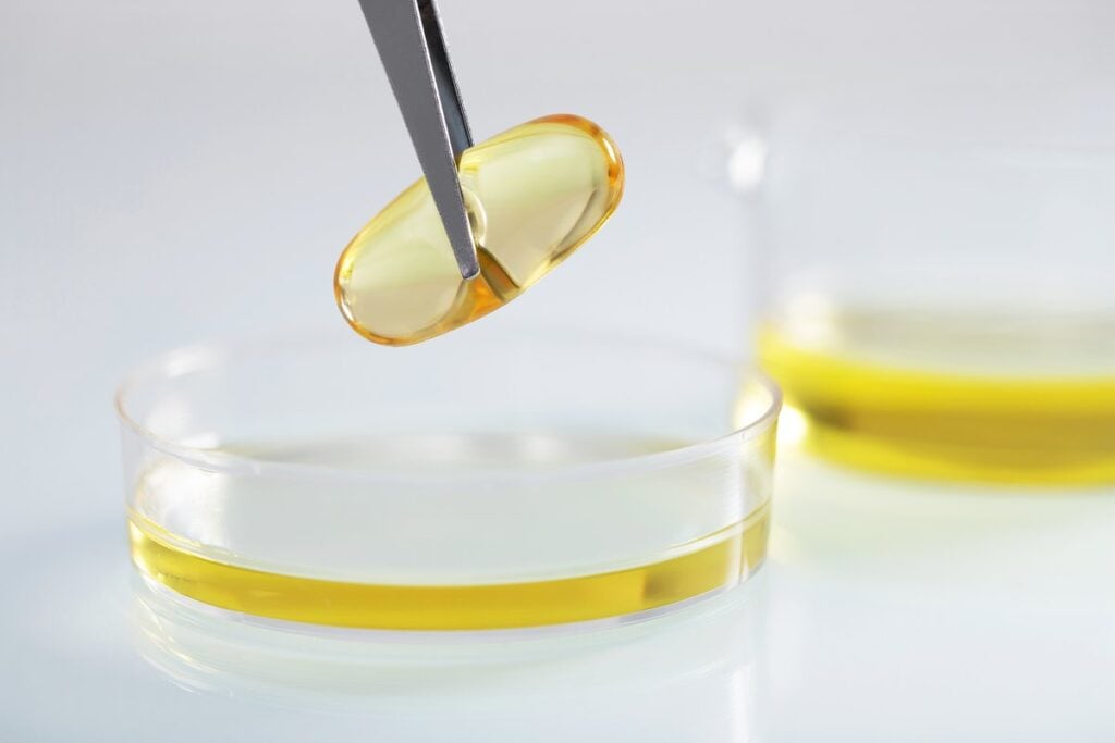 Tweezers holding a yellow capsule over oil in a laboratory dish