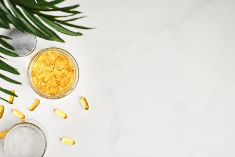Omega-3 capsules in a glass jar and scattered on a white surface