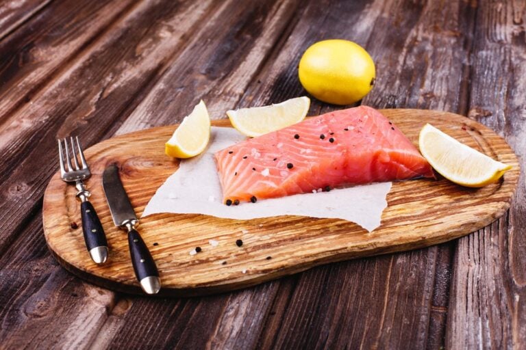 Raw salmon fillet with lemon halves on a wooden board